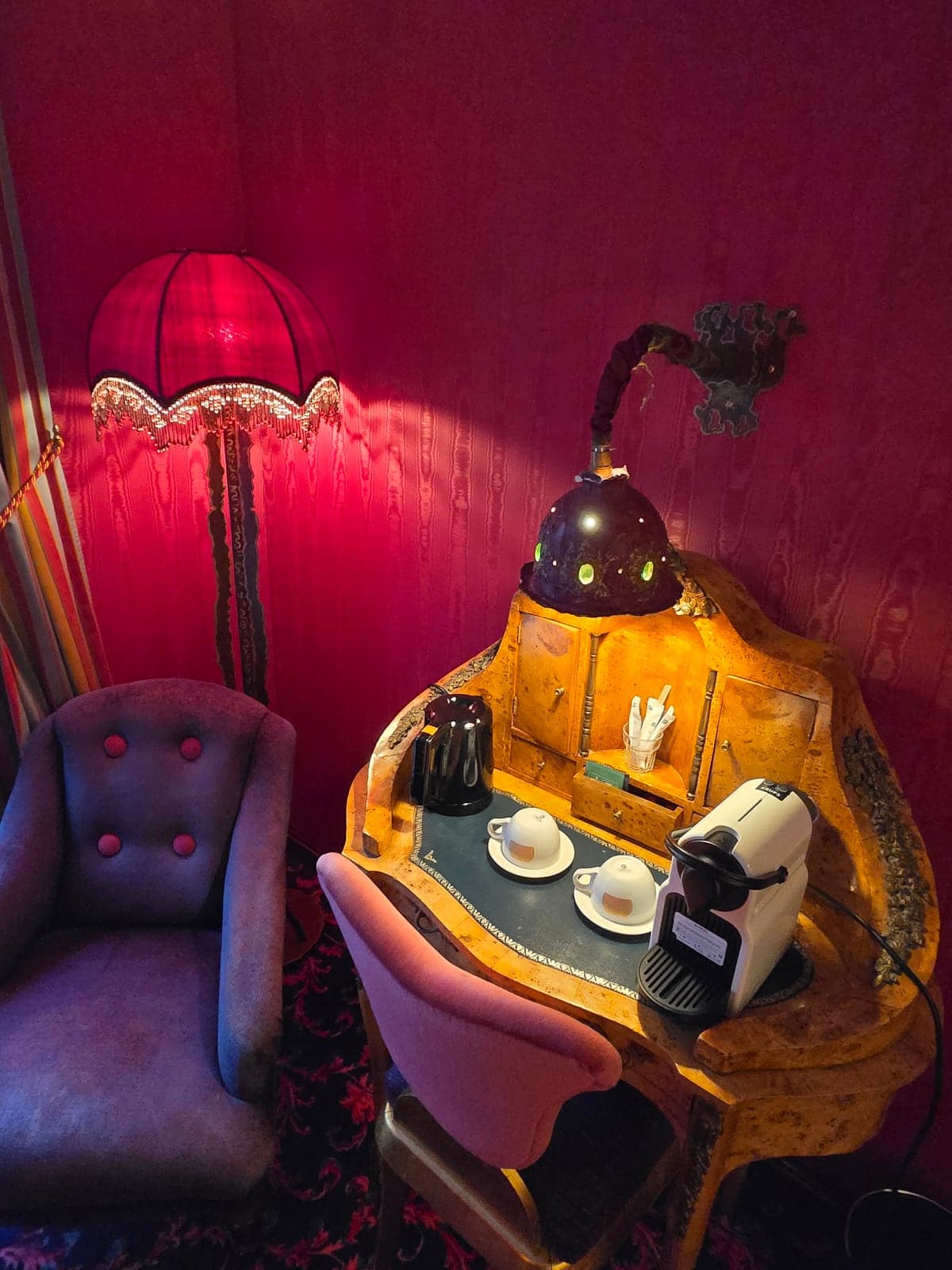 A glowing lamp on a small table against a deep red wall.