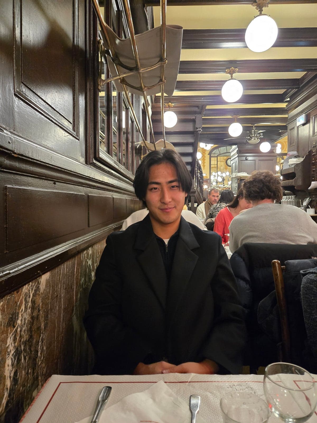 Max seated at a restaurant table beneath a row of globe lights.