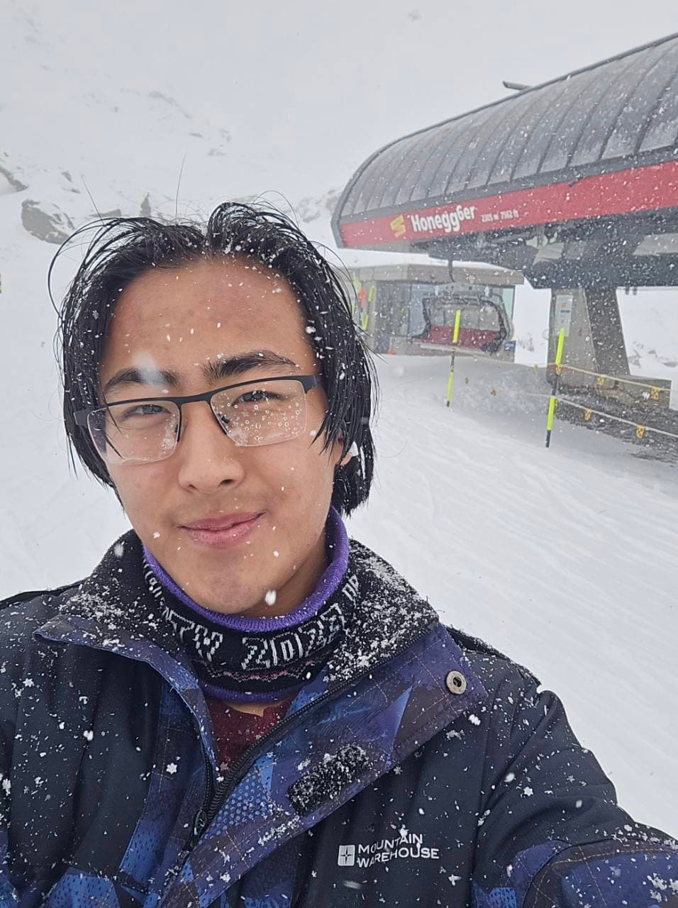 A smiling portrait in the snow beside a ski lift station.