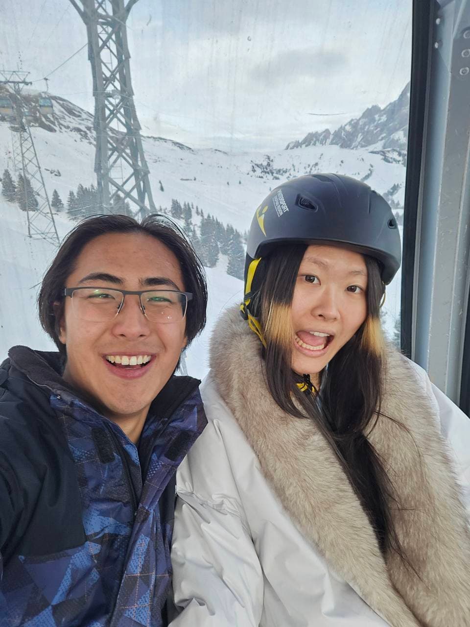 Two people smiling in a cable car above snowy slopes.